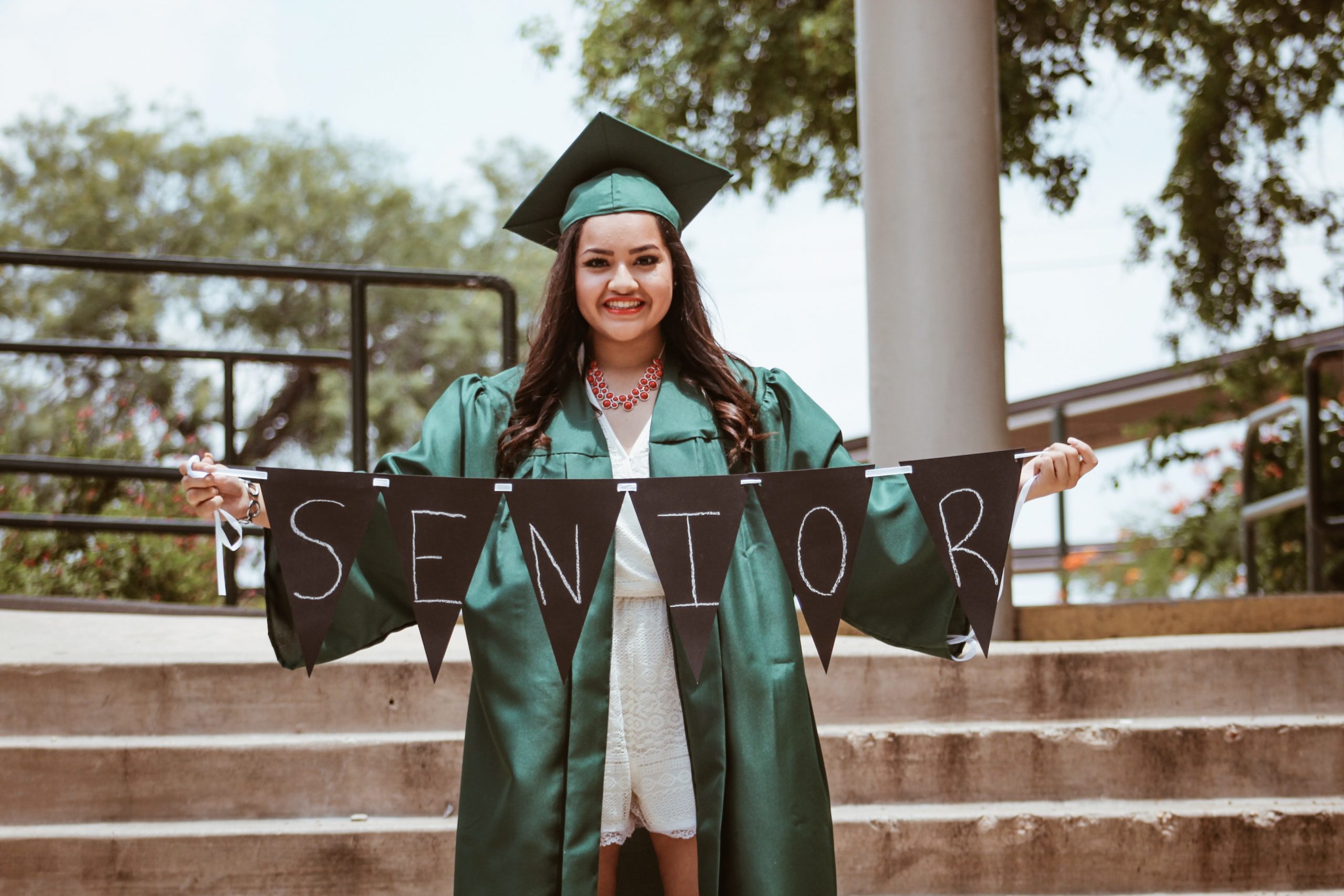 woman wearing graduation cap and gown holding a sign that says senior