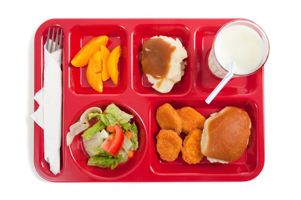 A red school lunch tray that contains chicken nuggets, salad, mashed potatoes, fruit and a carton of milk