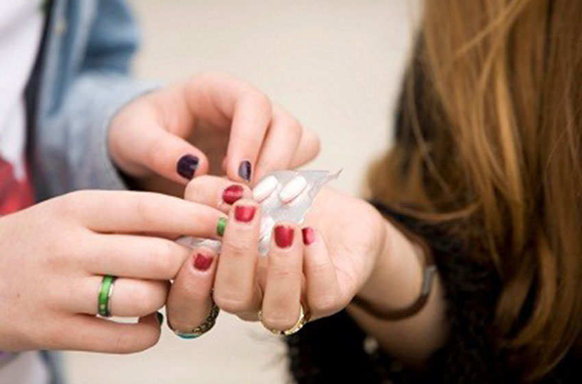 A close up shot of two students’ hands exchanging a pack of nondescript pills