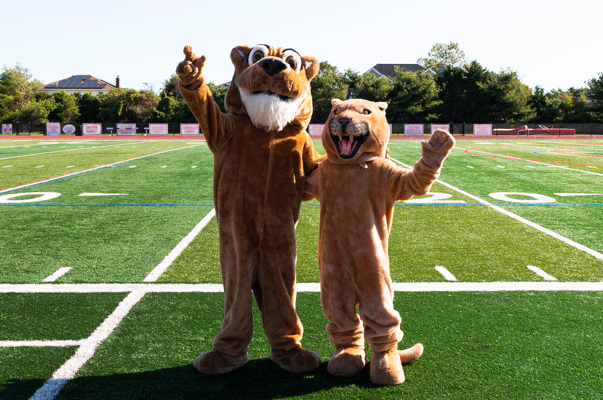 Two cougar mascots stand on a football field. They are waving at the camera
