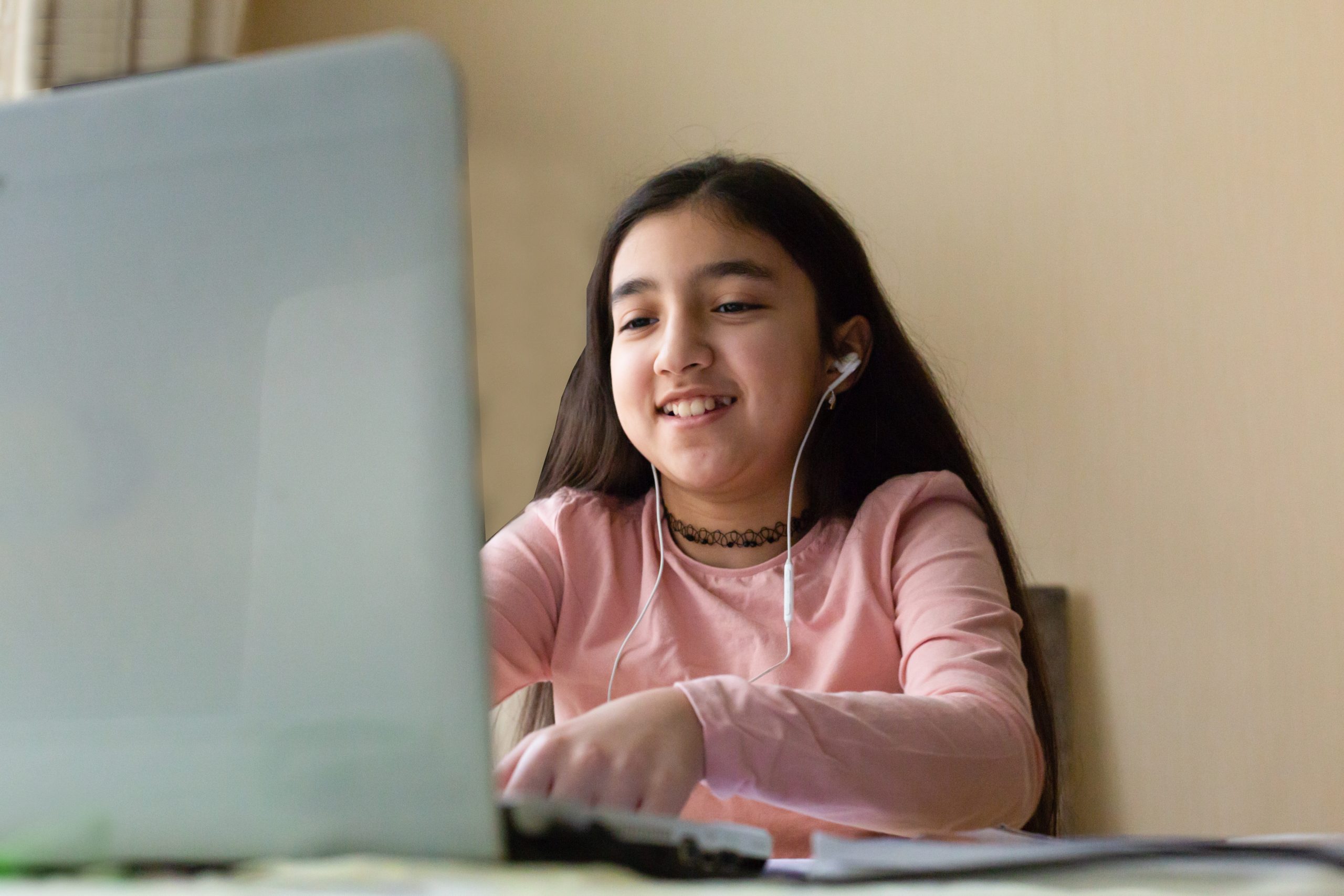 A student smiles while sitting in front of a laptop, wearing headphones