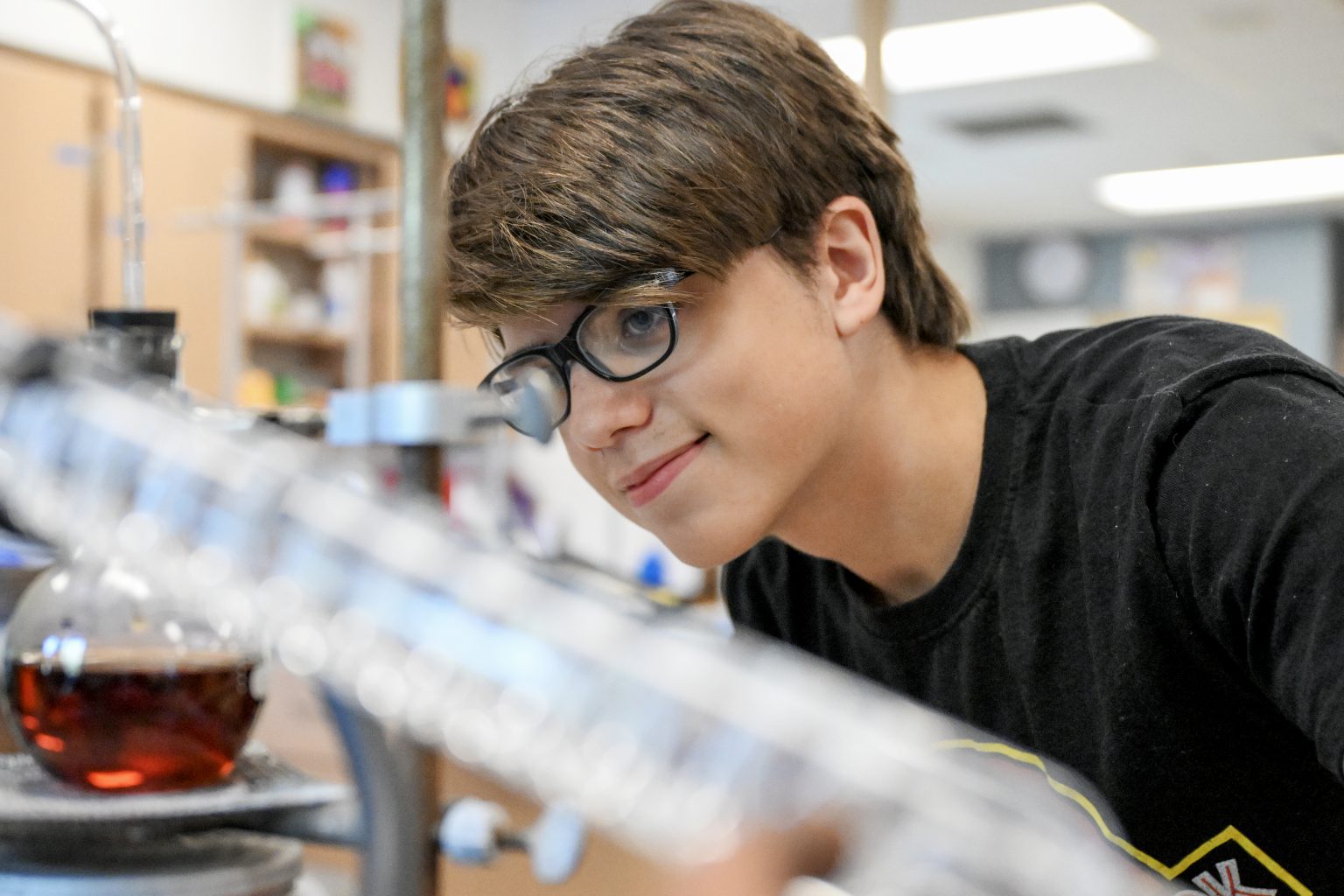 A young man with glasses and brown hair looks at science tools in a classroom.